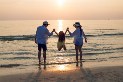 Rear view of men on beach against sky during sunset