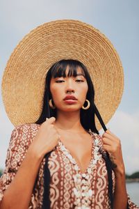 Portrait of young woman wearing hat standing at beach against sky