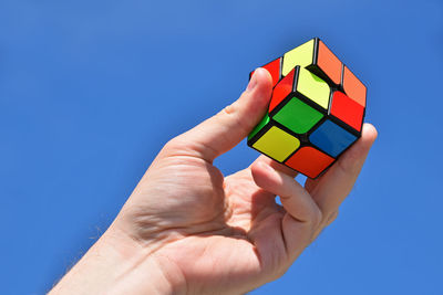 Close-up of hand holding puzzle cube against clear blue sky