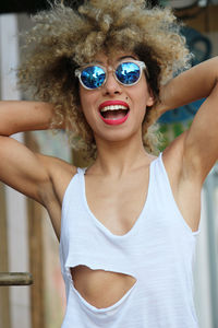 Smiling woman with curly hair wearing sunglasses standing in city on sunny day