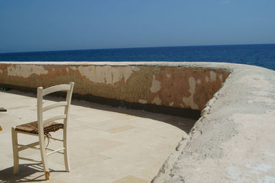 Chair on beach against clear blue sky