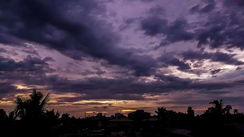 Silhouette trees and buildings against dramatic sky