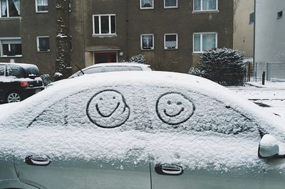 Anthropomorphic smiley face on snow covered windows of car 