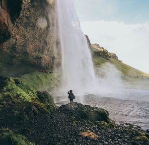 Woman looking at waterfall against sky
