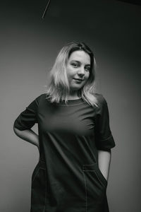 Portrait of young woman standing against gray background