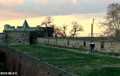 Rear view of man by building against sky during sunset