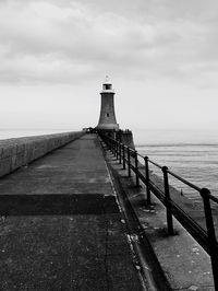 Pier leading towards lighthouse over sea against sky