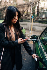 Long hair brunette asian woman opening a car with mobile phone