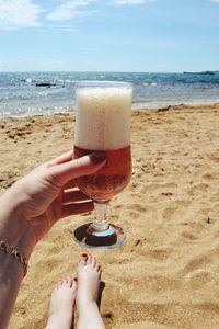 Close-up of woman holding beer glass against beach