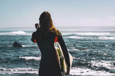 Rear view of woman standing on beach against sky