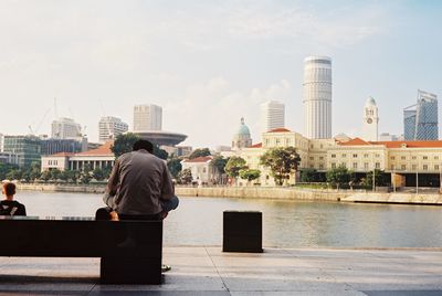 Rear view of man and river against buildings in city