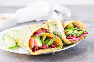 Egg rolls filled with pastrami, cucumber, radish and green onions on a plate on the table