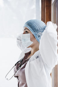 Female doctor in surgical cap adjusting protective face mask