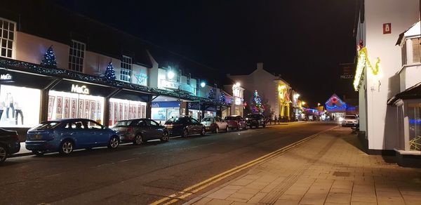 Illuminated street by buildings in city at night