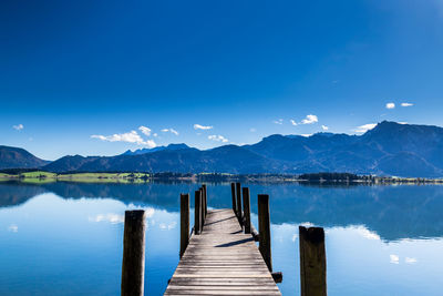 Wooden jetty on pier over lake against blue sky