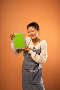 Young woman using digital tablet while standing against blue background