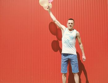 Man with balloons flying against red wall