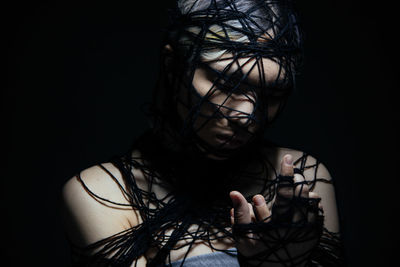 Fashion close-up of young girl with ropes like trapped against black background in studio