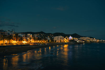 Illuminated buildings by river against sky