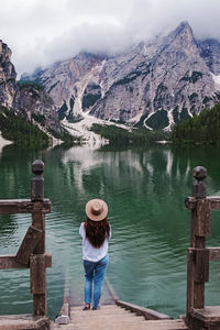 Woman traveler in a hat standing at the bank of beautiful lake braies, italy.