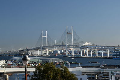 Suspension bridge over river in city against clear sky