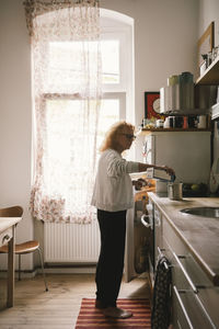 Side view of senior woman pouring milk in container while standing in kitchen at home