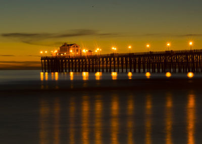 Illuminated building by sea against sky at night