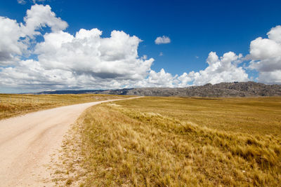 Empty road amidst field against sky
