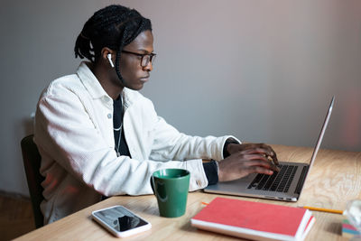 Young focused african american man sits at wooden table with laptop getting internet education