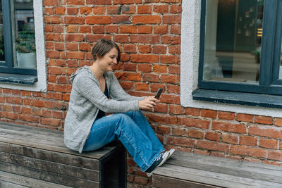 Portrait of young woman sitting against brick wall
