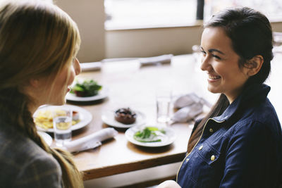High angle view of happy female friends talking while sitting at table in restaurant