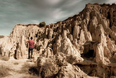 Rear view of man standing on rock formation against sky