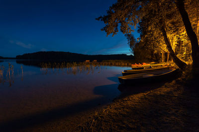 Boats moored on lake by trees against sky