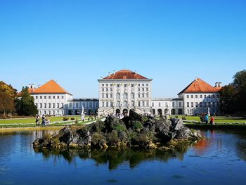 Buildings by pond against clear blue sky