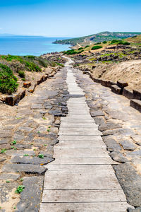 Footpath leading towards sea against clear sky