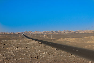 Tire tracks on desert against clear blue sky