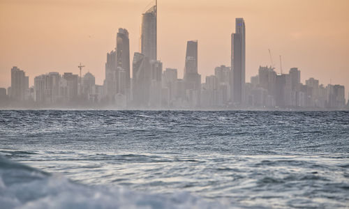 Sea by modern buildings in city against sky