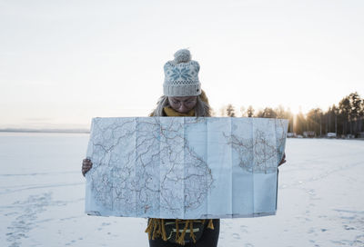 Woman holding a large map whilst standing on a frozen lake in sweden