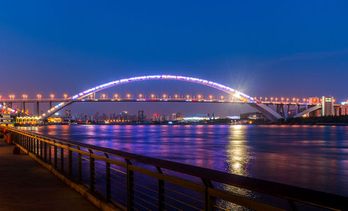 Illuminated bridge over river against sky at night