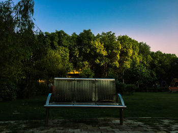 Empty chairs and table against trees against clear sky