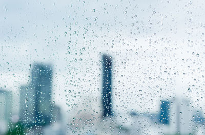 Rain drop on glass window at day time in monsoon season with blurred city buildings background.