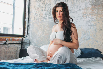 Portrait of pregnant woman sitting on bed at home