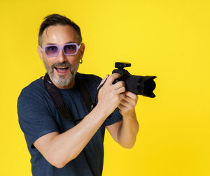 Portrait of young man with camera against yellow background