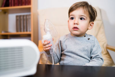 Cute boy looking away while holding respiratory mask at home