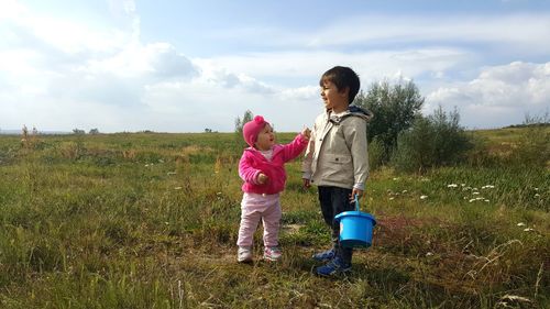 Siblings standing on field against sky