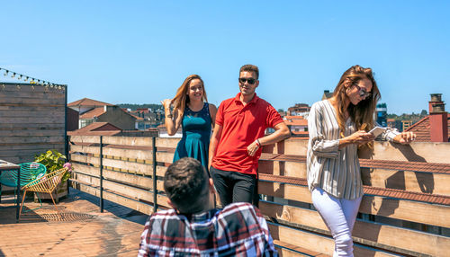 Happy friends talking in rooftop city while woman looking her phone