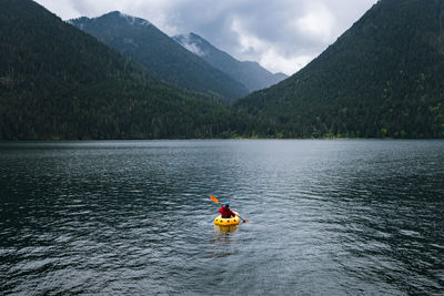 Person in kayak paddling on lake towards mountains