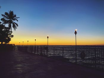 Street lights on footpath by sea against clear sky