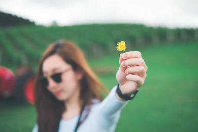 Young woman holding small yellow flower while standing on field