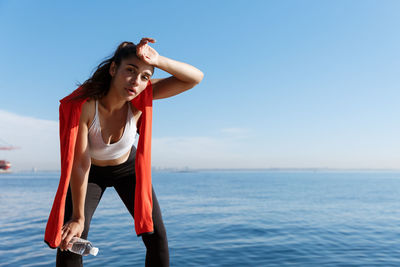 Portrait of tired young woman standing against sea